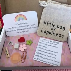 a little bag of happiness sits in a cardboard box with other items on it, including keychains and buttons