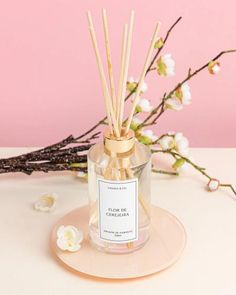 a small glass bottle filled with reeds next to white flowers on a pink plate