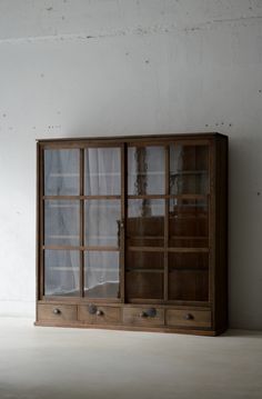 an old wooden cabinet with glass doors on the front and side, against a white wall