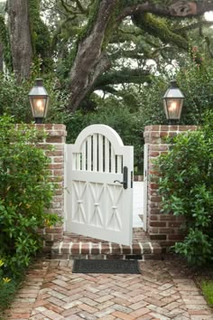 a white gate with two lights on each side and a brick path leading to it