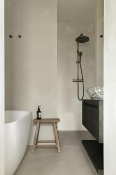 a white bathroom with a wooden bench in the corner and a shower head on the wall