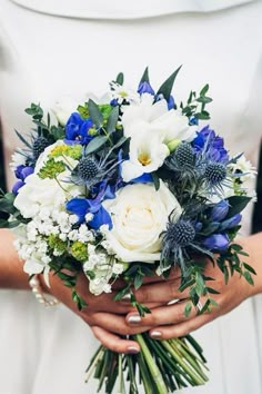 a bride holding a bouquet of white and blue flowers with greenery in her hands