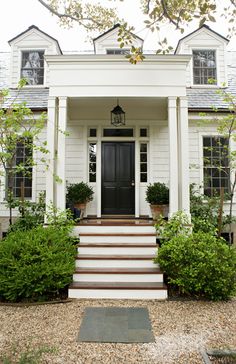 a white house with steps leading up to the front door and entry way that is surrounded by shrubbery