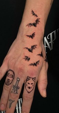 a person's hand with tattoos on it and some bats flying above the fingers