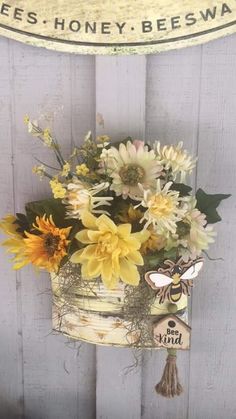 a vase filled with yellow and white flowers sitting on top of a wooden table next to a sign