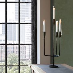 three candles are lit on a table in front of a window with cityscape