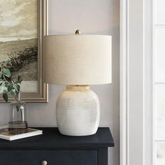 a white vase sitting on top of a black table next to a lamp and a painting