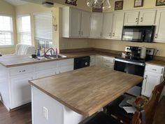 a kitchen with white cabinets and wood counter tops, an island in front of the stove