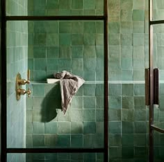 a green tiled bathroom with a towel hanging on the wall