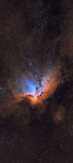 an orange and blue star surrounded by stars in the night sky, with dark clouds