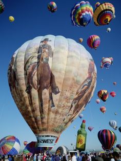 many hot air balloons flying in the sky with horses on them and people looking at them