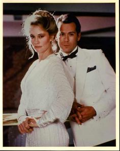 a man and woman dressed in white posing for a photo with their arms around each other