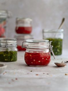 several jars filled with different types of food and spoons next to eachother