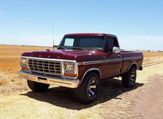 an old red pickup truck parked on the side of a dirt road in a field