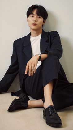 a young man sitting on the floor wearing a suit and black shoes with his legs crossed