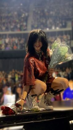 a woman sitting on top of a piano in front of a crowd holding onto flowers