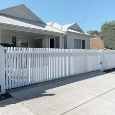 a white picket fence in front of a house with a car parked on the driveway