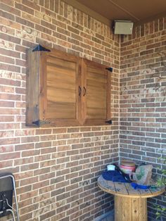 a wooden table sitting in front of a brick wall with shutters on the windows