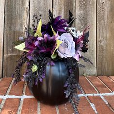 a black vase filled with purple and white flowers on top of a wooden table next to a fence