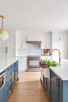 a kitchen with white and blue cabinets, an island countertop and gold pendant lights