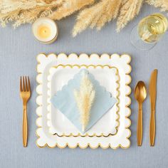 a place setting with napkins, forks and candles on a blue table cloth next to wheat stalks