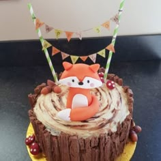 a birthday cake decorated with a fox on top of a tree stump and bunting flags