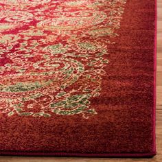 a red area rug with an ornate design on the top and bottom, sitting on a wooden floor