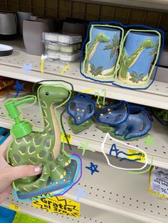 a person holding a green dinosaur toy in front of some other items on a shelf