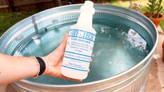 a hand holding a bottle of disinfectant in front of a metal barrel