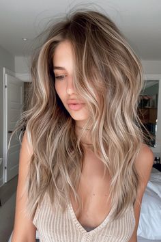 Woman with long, wavy blonde hair posing in a softly lit room. Blonde On Light Brown Hair, Fall Hair For Natural Blondes, Low Maintenance Highlights Blondes, Blonde Hair For Fall Low Lights, Natural Blonde Fall Hair Color, Soft Brown With Blonde Highlights, Brunette Blonde Highlights And Money Pieces, Fall Blonde Hair Color Dark Roots, Blonde With Heavy Lowlights