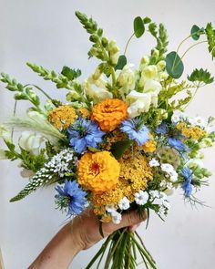 a person holding a bouquet of flowers in their hand with white, yellow and blue flowers