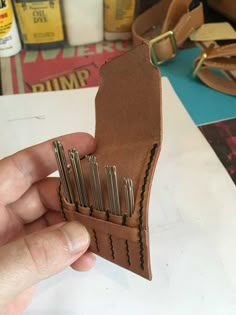 a person holding up a leather wallet with many screwdrivers in it and some other tools on the table