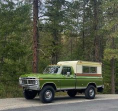 an old green truck with a camper on the back parked in front of some trees