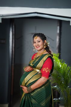 a woman in a green and red sari standing with her arms on her hips