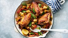 a pan filled with chicken and potatoes on top of a blue table cloth next to a spoon