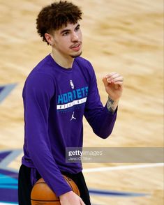 a young man holding a basketball while standing on top of a basketball court with his hand up