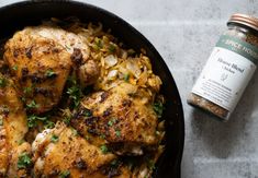 a pan filled with chicken and rice next to a jar of spice