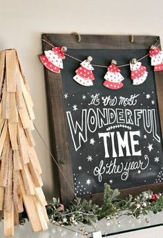 a chalkboard sign with christmas decorations on it next to a small tree and wooden logs