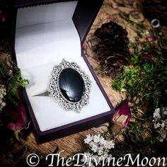 an oval black stone ring sits in a box surrounded by flowers and pineconis