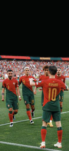 the soccer players are playing on the field in red and green uniforms, with their arms around each other