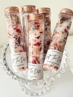 four jars filled with different types of sea salts on a glass platter next to pearls