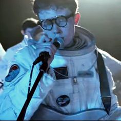 a man in an astronaut suit singing into a microphone with another man standing behind him