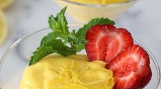 two glasses filled with fruit on top of a white marble counter topped with lemon custard and sliced strawberries