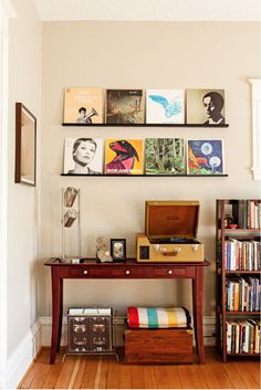 there are many pictures on the wall above this desk and bookshelf in this room