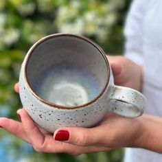 a woman holding a cup in her hand with red nail polish on the thumbnails