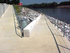 a concrete walkway next to a body of water with rocks on the side and trees in the background