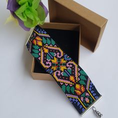 a colorful beaded bracelet in a box next to a flower