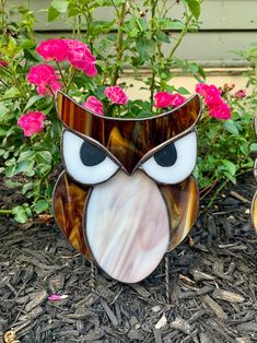 an owl statue sitting on top of a flower bed next to a bush with pink flowers