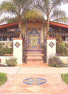 an entrance to a home with palm trees in the foreground and colorful tile work on the front door