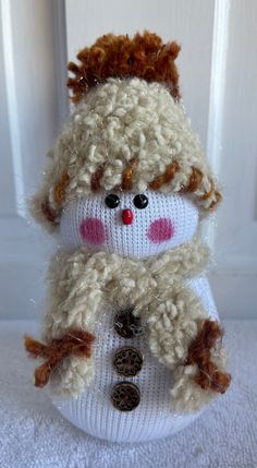 a white knitted snowman sitting on top of a table next to a door